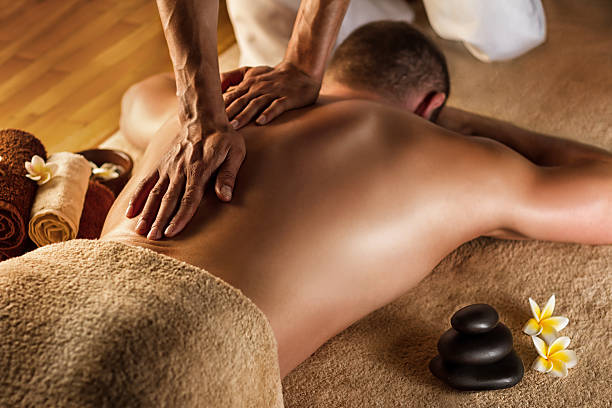 man has deep tissue massage on the back. spa stones and frangipani flowers.